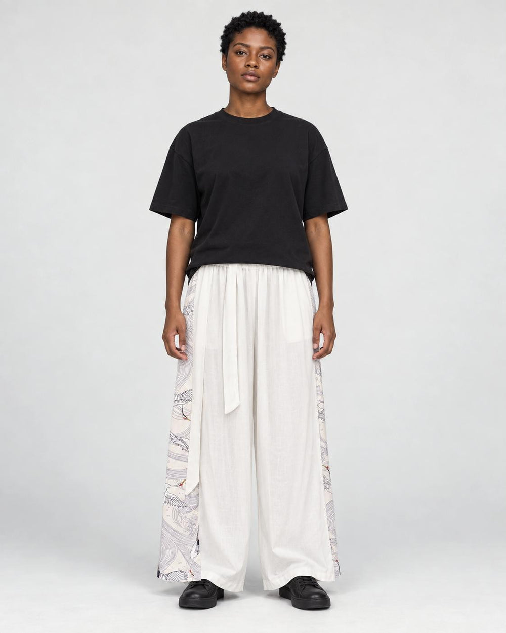 Model wearing the white wide-leg pants with pale gray crane and wave side panels and a black tee, front view