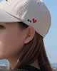 Close-up of the small red heart with H.G lettering embroidered on the side of the beige cap