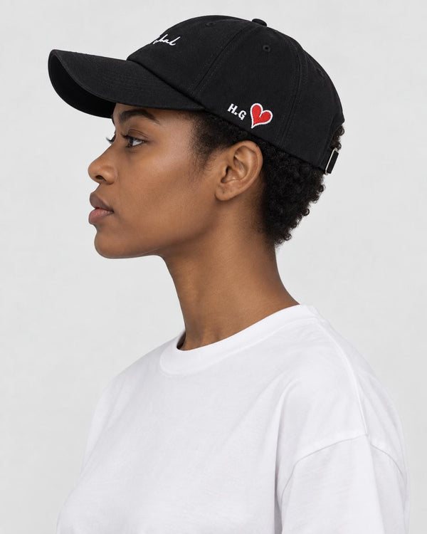 Model wearing the black cursive script cap with a white tee, side view