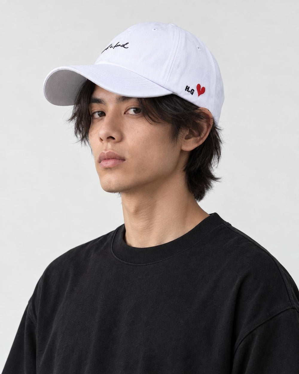 Model wearing the white cursive script cap with a black tee, three-quarter view
