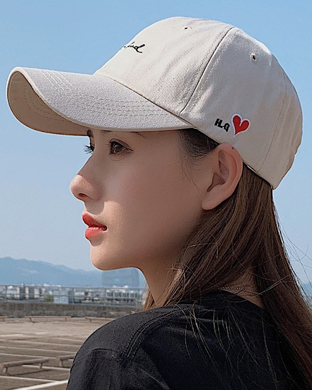 Woman wearing the beige cap with black cursive script and a small red heart on the side, profile view