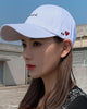 Woman wearing the white cap with black cursive script and a small red heart on the side, three-quarter view