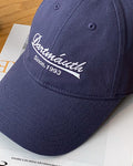 Close-up of the raised cursive script embroidery on the navy blue cap
