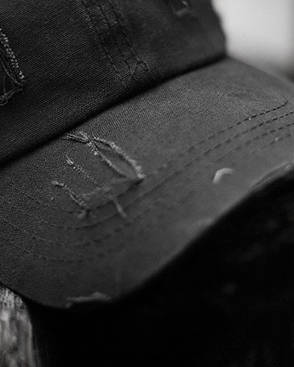 Close-up of the stitched and frayed brim of the black cap