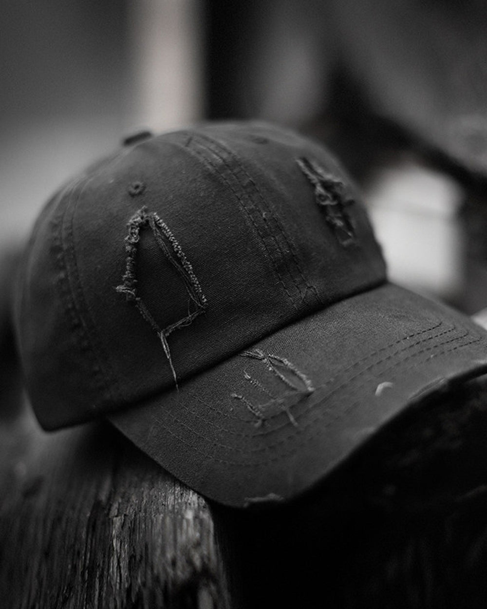 Black distressed baseball cap resting on a dark post, showing the frayed holes on the crown and brim