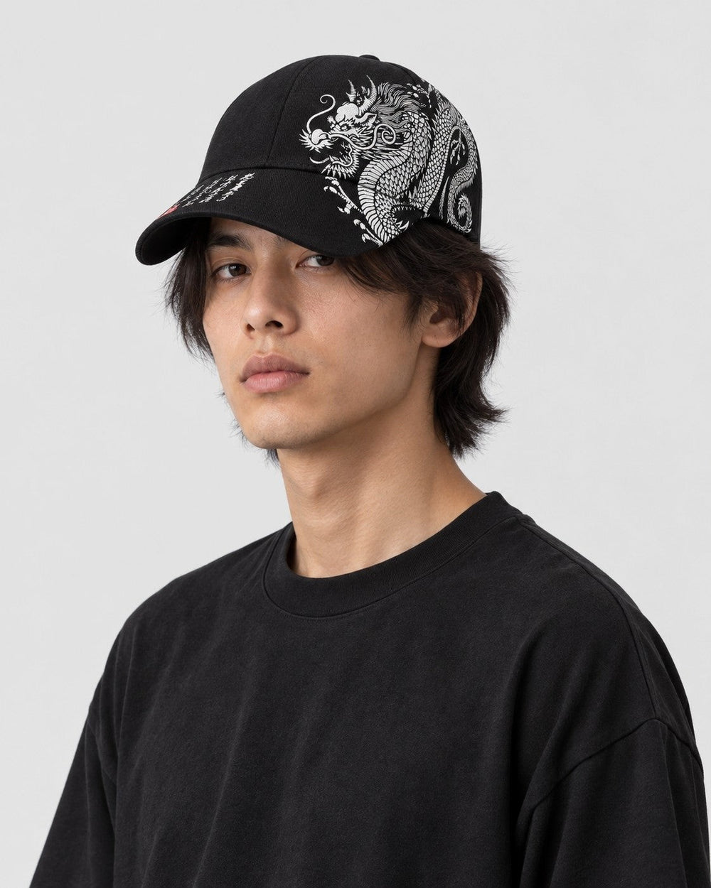 Man wearing the black dragon print cap with a plain black tee, the dragon on the left side of the crown