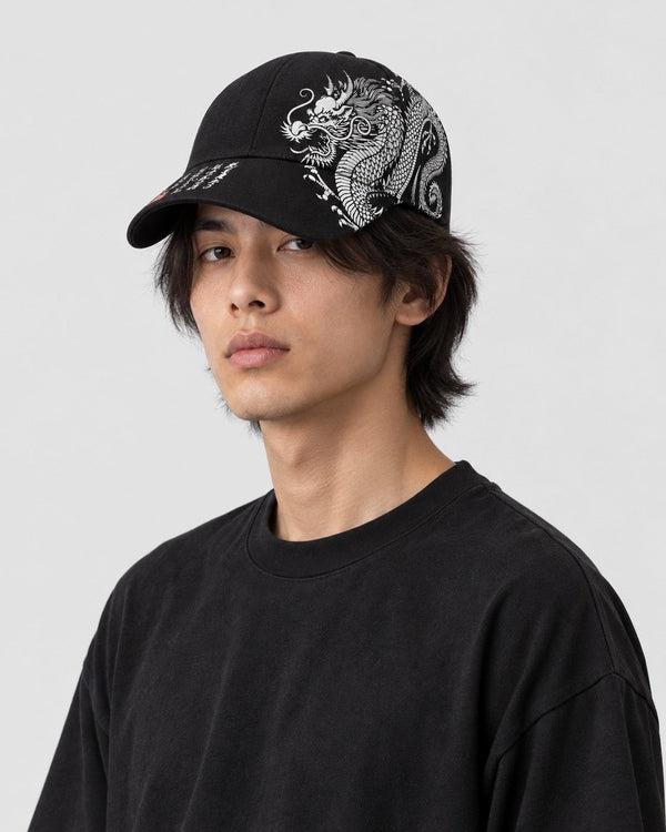 Man wearing the black dragon print cap with a plain black tee, the dragon on the left side of the crown