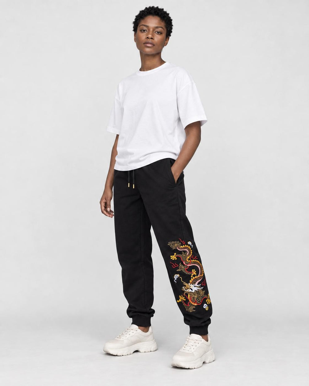 Model wearing the black dragon embroidered jogger pants with chunky sneakers, three-quarter view