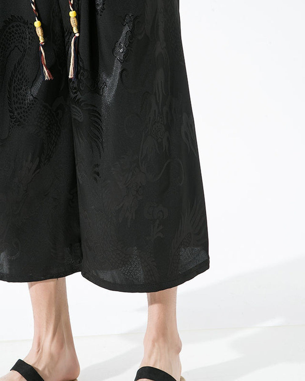 Close-up of the glossy black dragon-and-cloud jacquard and the drawcord tassels on the pants