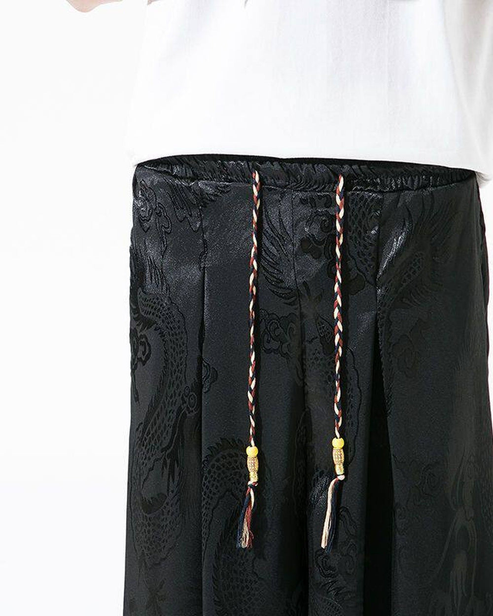 Close-up of the elastic waist, front pleats and braided drawcord with yellow beads and tassels on the black pants
