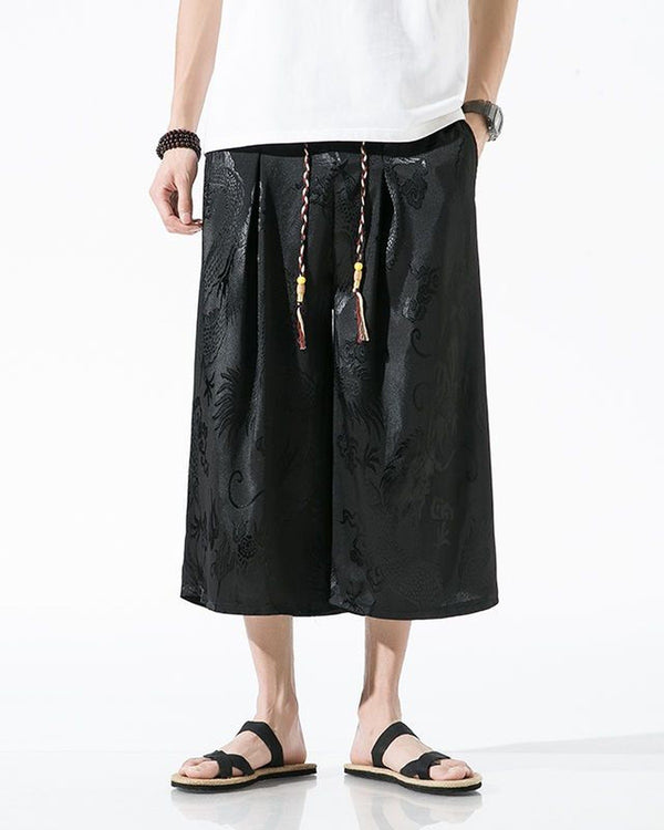 Black dragon jacquard wide-leg pants with front pleats and a beaded, tasseled drawcord, worn with a white tee