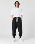 Model wearing the black drop-crotch harem pants with a white tee, front view