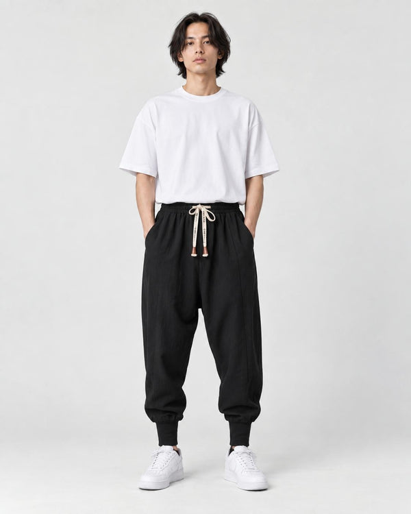 Model wearing the black drop-crotch harem pants with a white tee, front view