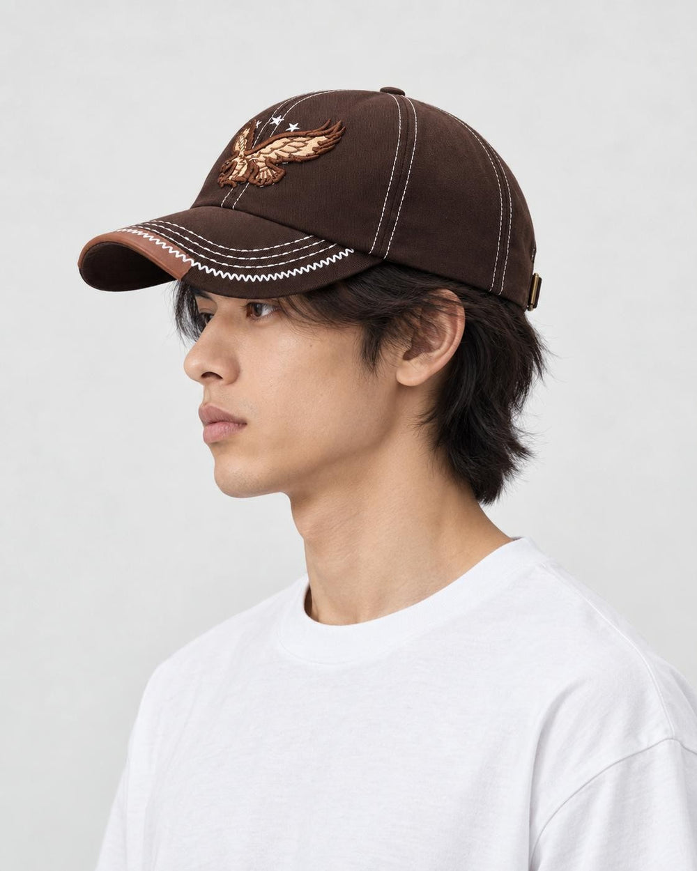 Model wearing the brown eagle cap, side view of the stitched brim