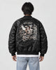 Model seen from behind in the black padded bomber jacket with a cream eagle and map embroidery, a white tee and light jeans