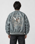 Model seen from behind in the slate gray padded bomber jacket with a cream eagle and map embroidery and black jeans