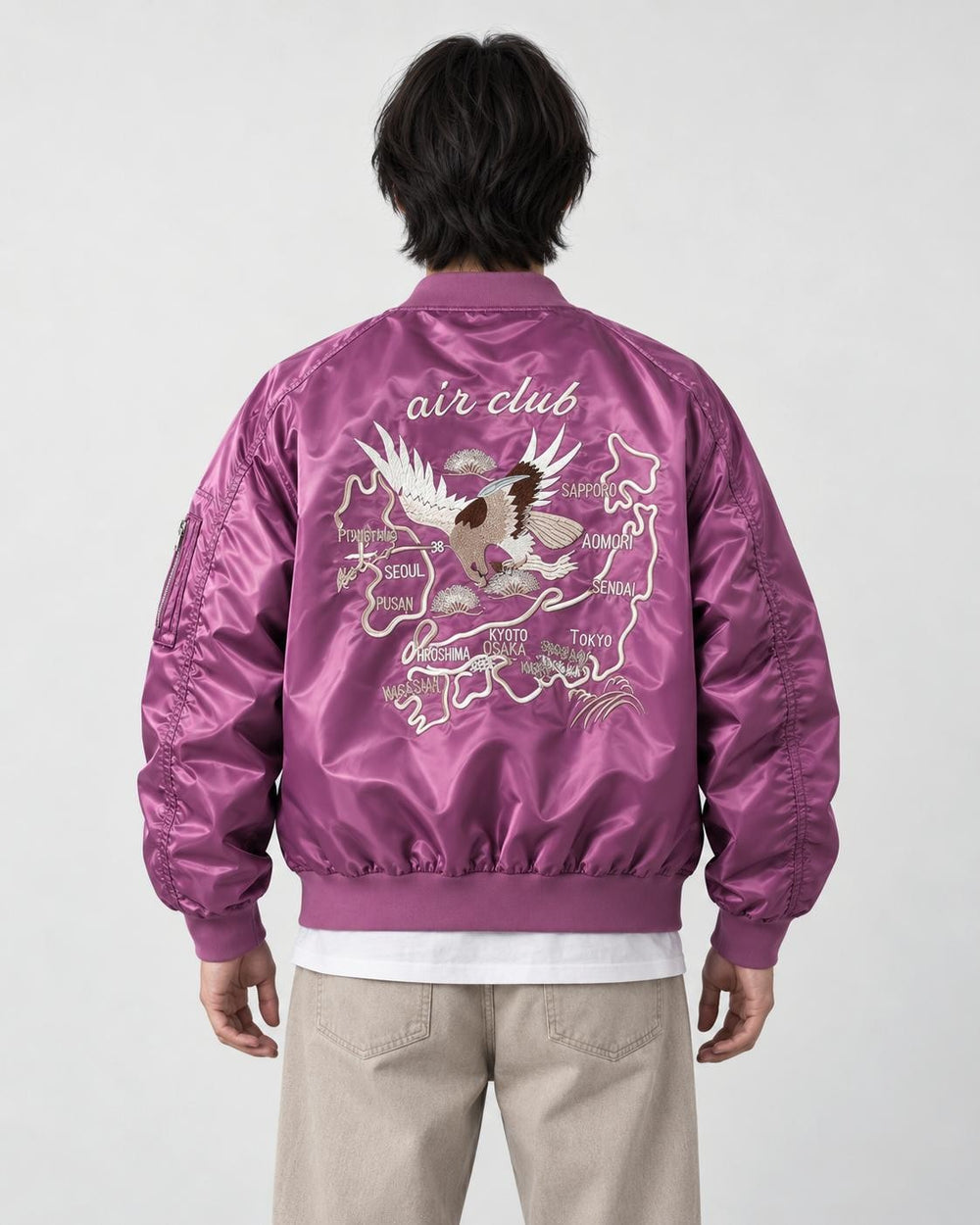 Model seen from behind in the purple padded bomber jacket with a cream eagle and map embroidery and stone trousers