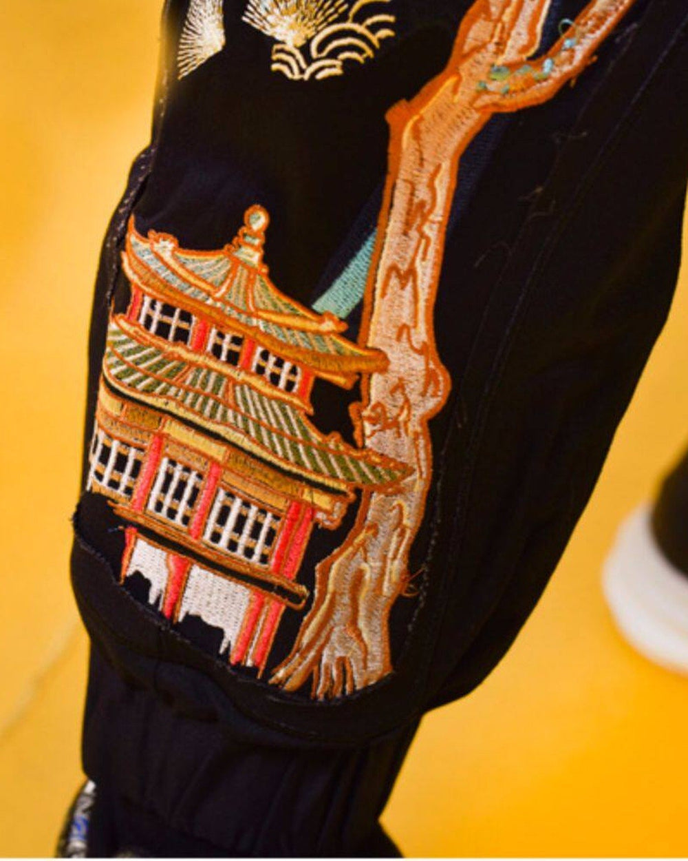Close view of the embroidered two-storey pavilion with a red and gold roof above the ankle cuff