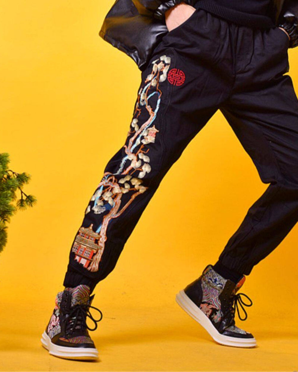 Model in mid-stride in the black joggers, with the pine tree embroidery running from the red seal to the pavilion
