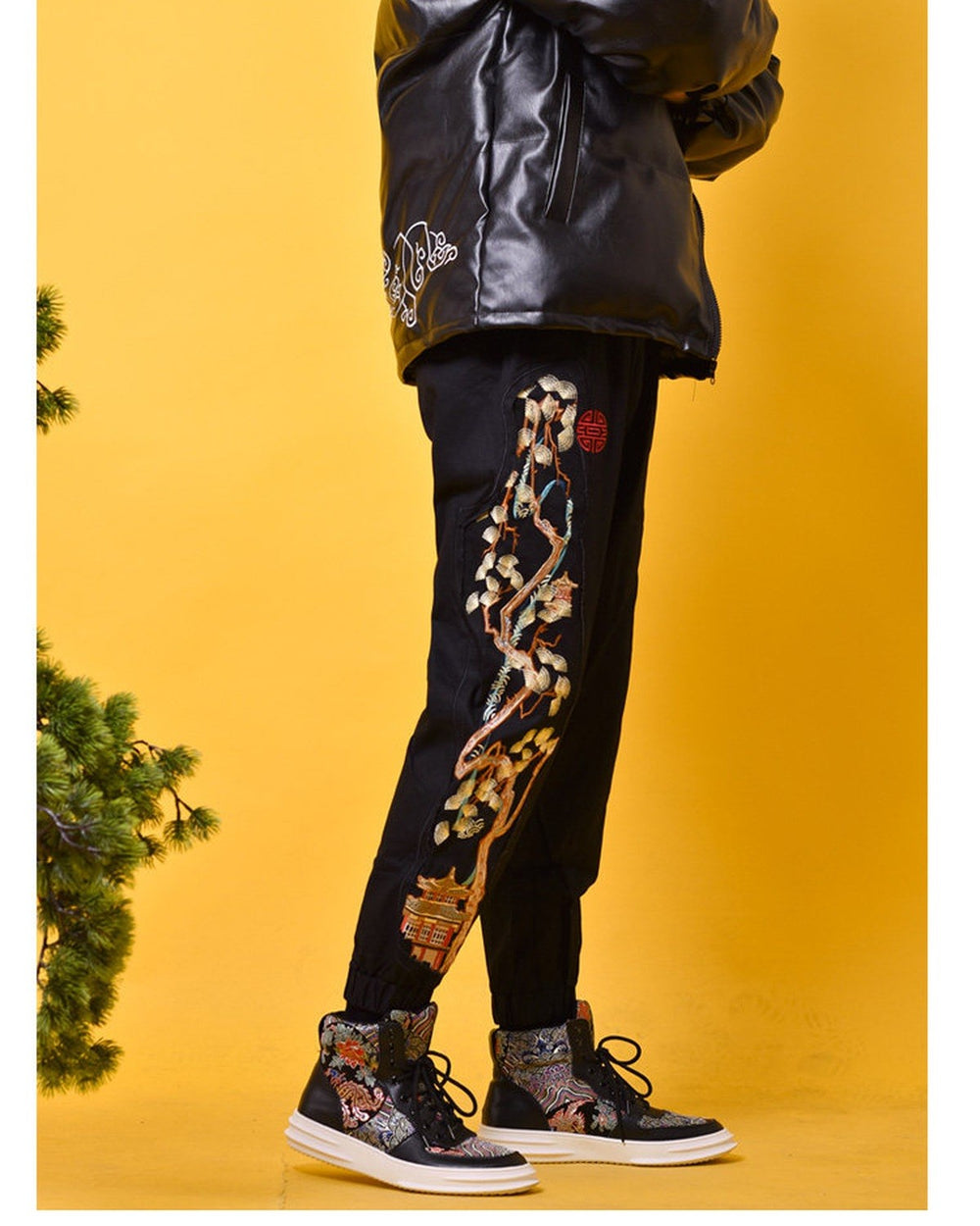 Black joggers worn standing with the pine tree and pavilion embroidery on the outer leg and elastic cuffs