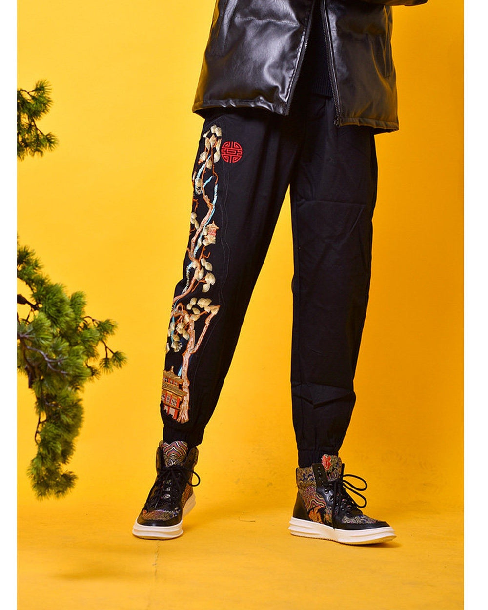 Front view of the black joggers with the embroidered pine tree down one leg and a small red seal at the hip