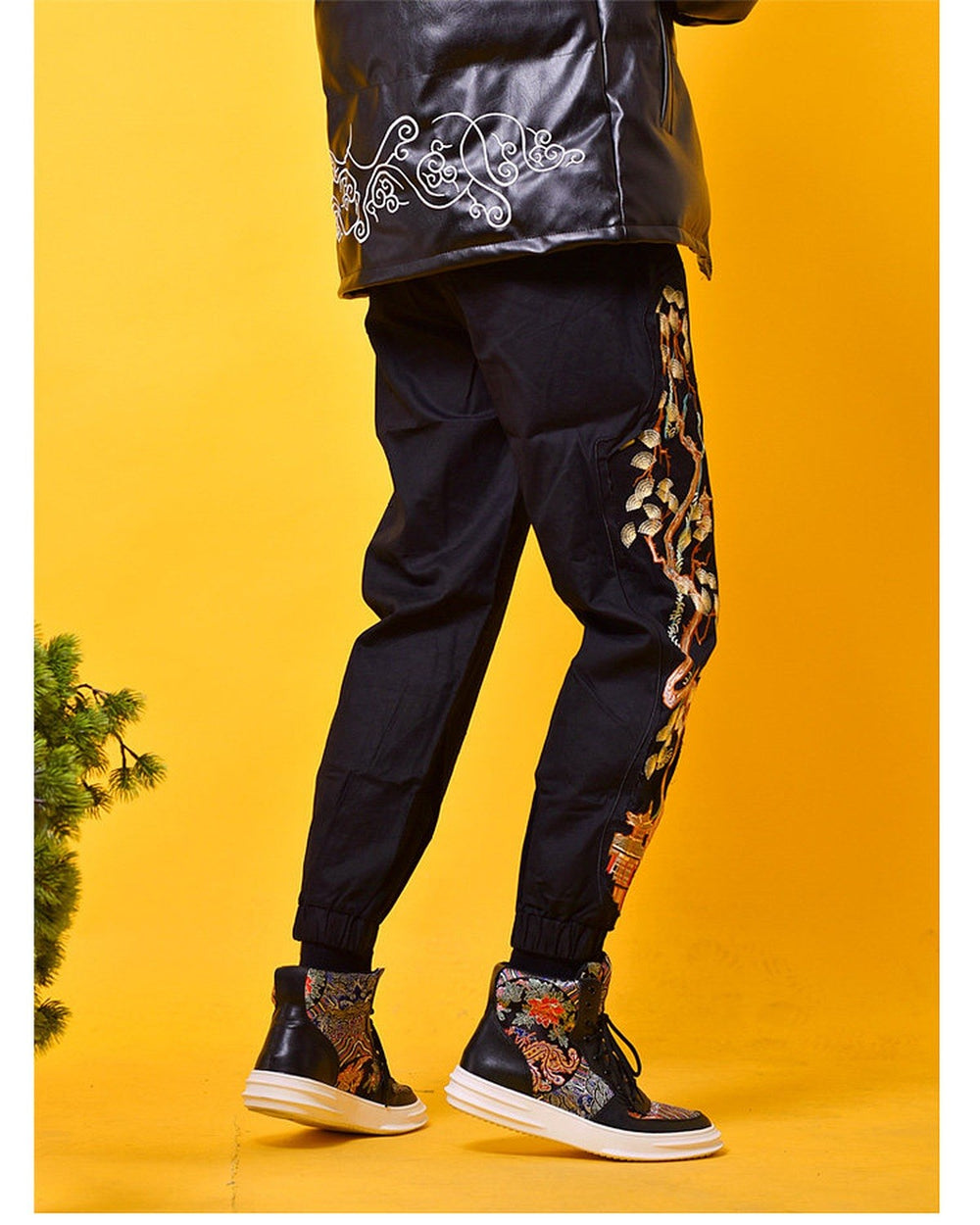 Black joggers worn with ankle boots, the pine tree embroidery and the pavilion visible on the outer leg