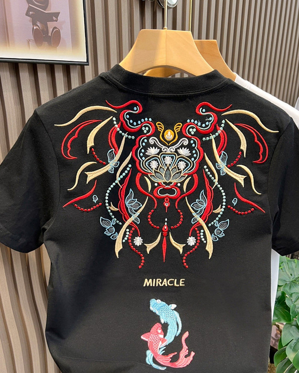 Back of the black T-shirt with a red, gold and teal embroidered mask, the word MIRACLE and two koi