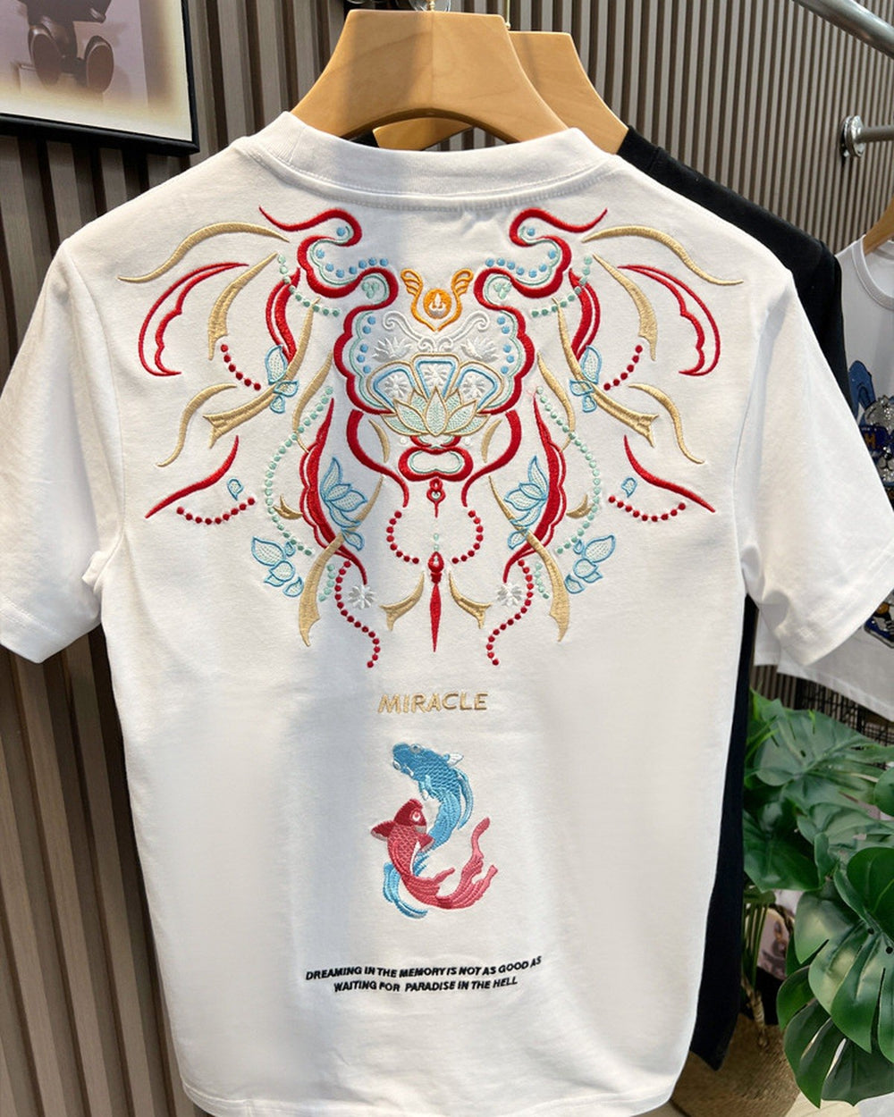 Back of the white T-shirt with a red, gold and teal embroidered mask, the word MIRACLE and a teal and a coral koi
