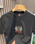 Front of the black T-shirt with a small embroidered MIRACLE emblem at the chest and a red label at the neck