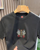 Front of the black T-shirt with a small embroidered MIRACLE emblem at the chest and a red label at the neck
