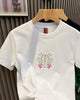 Front of the white T-shirt with a small embroidered MIRACLE emblem at the chest and a red label at the neck