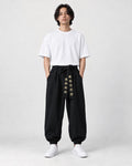 Model wearing black harem pants with a gold-embroidered sash, a white tee and white sneakers, front view