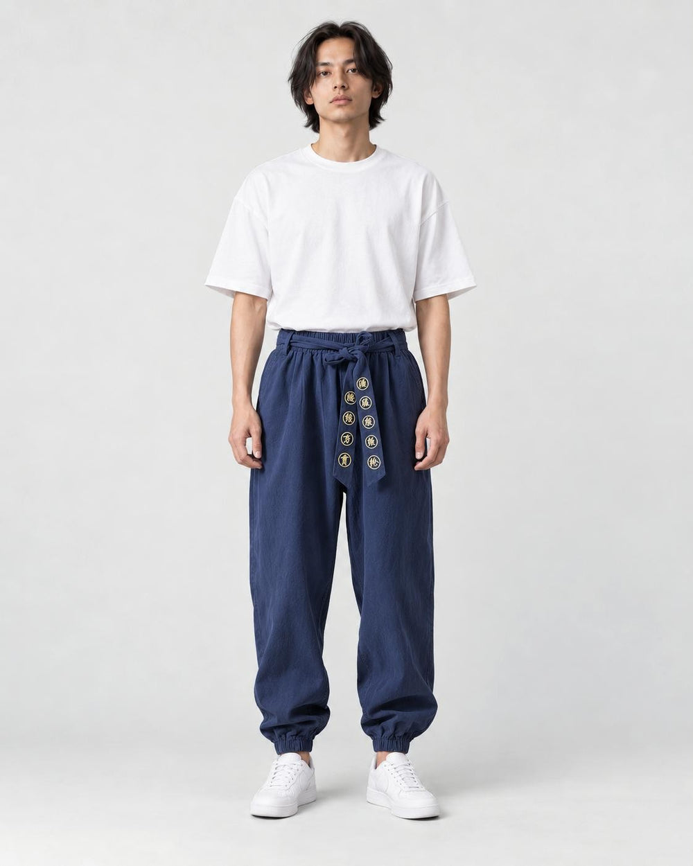 Model wearing navy harem pants with an embroidered sash and a white tee, front view