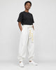 Model wearing white harem pants with a cream sash and a black tee, three-quarter view