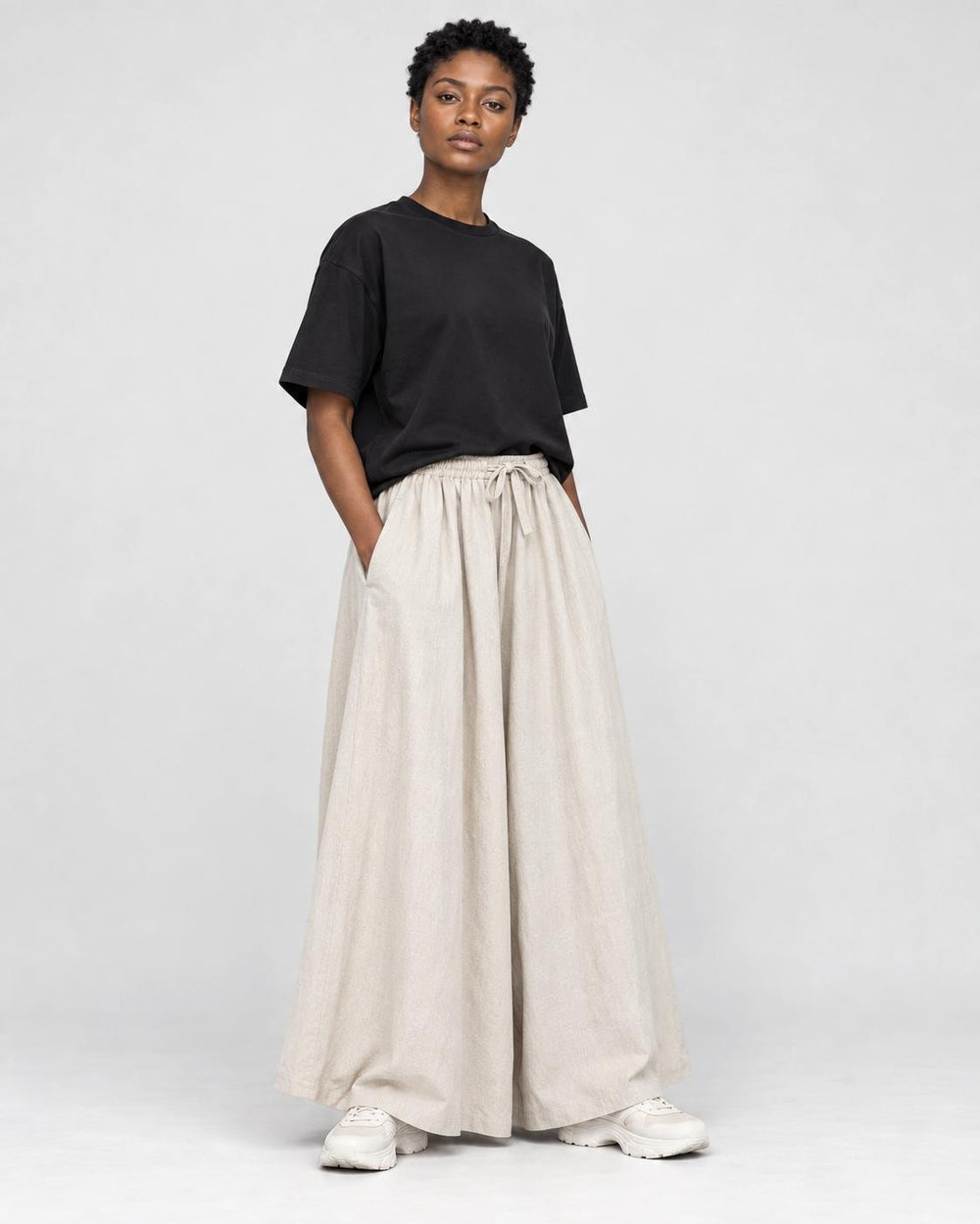 Model wearing the cream extra-wide linen-cotton skirt pants with a black tee and white sneakers, three-quarter view
