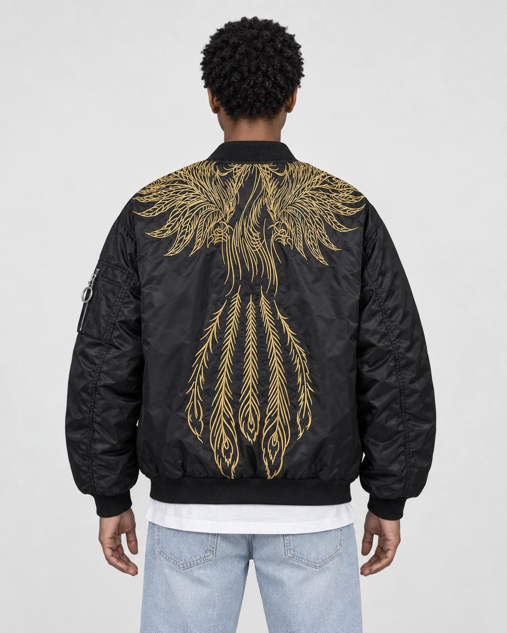 Model wearing the black bomber jacket with gold wing embroidery and light-wash jeans, back view