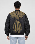 Model wearing the black bomber jacket with gold wing embroidery and light-wash jeans, back view