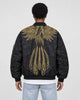 Model wearing the black bomber jacket with gold wing embroidery and light-wash jeans, back view
