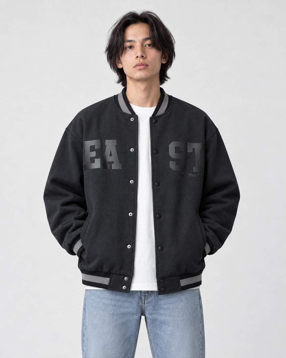 Model wearing the dark slate-black fleece-lined varsity jacket open over a white tee and light-wash jeans, front view
