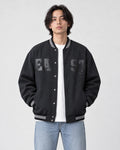 Model wearing the dark slate-black fleece-lined varsity jacket open over a white tee and light-wash jeans, front view