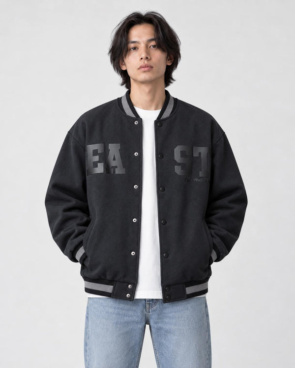 Model wearing the dark slate-black fleece-lined varsity jacket open over a white tee and light-wash jeans, front view