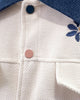 Close-up of the textured cream fabric, navy and pink snap buttons and blue collar