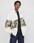 Model wearing the white floral tapestry patchwork shirt jacket open over a black tee, three-quarter view