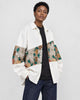 Model wearing the white floral tapestry patchwork shirt jacket open over a black tee, three-quarter view