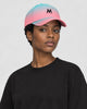 Woman wearing the aqua to pink gradient baseball cap with a black M, three-quarter view