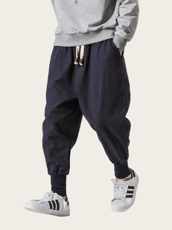 Person wearing black baggy pants with a gray sweatshirt and white sneakers on a white background