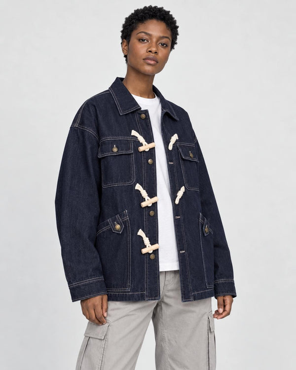 Model wearing the dark indigo horn toggle denim jacket over a white tee and stone trousers, three-quarter view