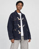 Model wearing the dark indigo horn toggle denim jacket over a white tee and stone trousers, three-quarter view
