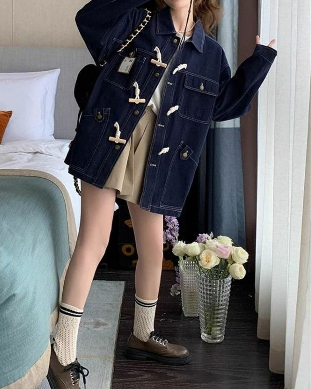 Full-length view of the dark indigo horn toggle denim jacket worn with a pleated beige skirt and brown lace-up shoes