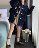 Full-length view of the dark indigo horn toggle denim jacket worn with a pleated beige skirt and brown lace-up shoes